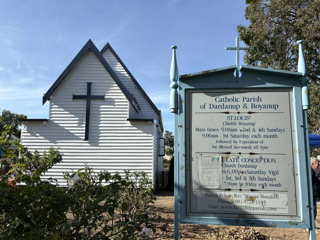 Historic Catholic church building with a signboard in front, blue sky background.
