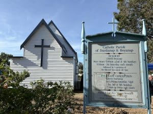 Historic Catholic church building with a signboard in front, blue sky background.
