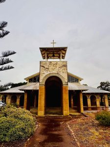 Bunbury Catholic Diocese church with cross on top, surrounded by greenery.