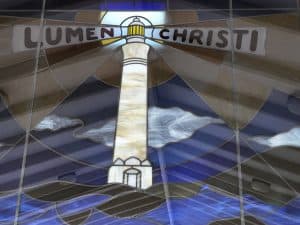 Stained glass window of a lighthouse with 'Lumen Christi' inscription.