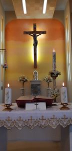 Interior of a Catholic church altar with crucifix, candles, and floral arrangements.