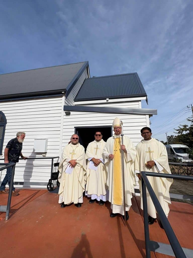 Catholic clergy standing outside Bunbury church building in sunny weather.