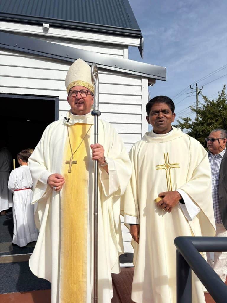Catholic clergy members in ceremonial robes outside church building.