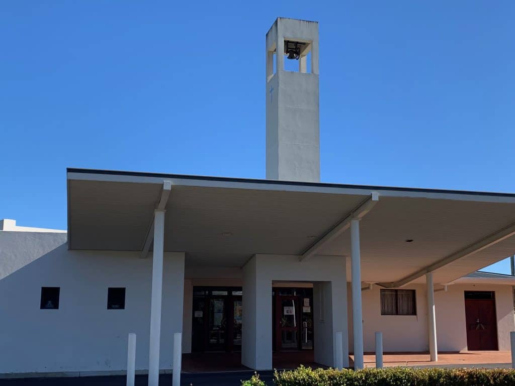 Modern church building with a tall bell tower under a clear blue sky.