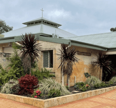 Exterior view of Bunbury Catholic Diocese church with garden and palm trees.